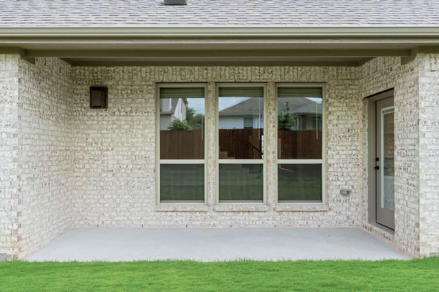 Covered back patio with concrete slab, light brick exterior, triple windows, and a side entry door Covered back patio with concrete slab, light brick exterior, triple windows, and a side entry door