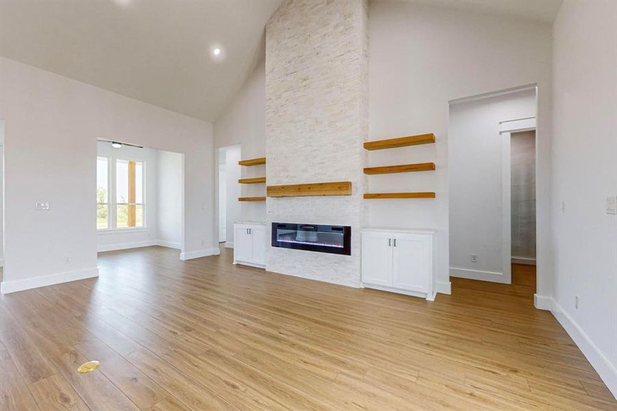 Unfurnished living room with light hardwood / wood-style flooring, a stone fireplace, and high vaulted ceiling