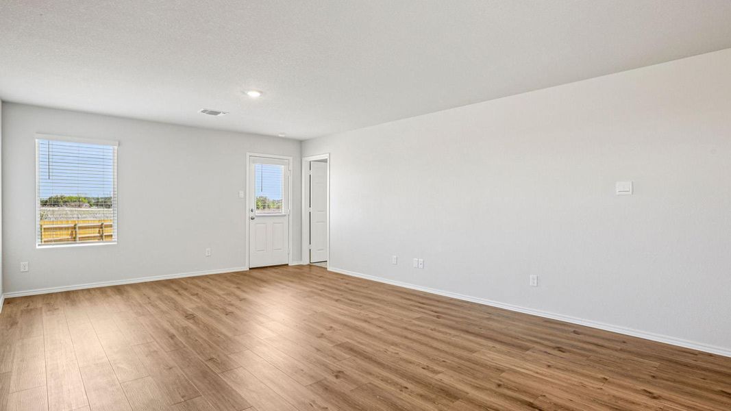 Spacious interior room featuring wood-finish flooring, light-toned walls, a window with blinds, and a door with a glass pane Spacious interior room featuring wood-finish flooring, light-toned walls, a window with blinds, and a door with a glass pane