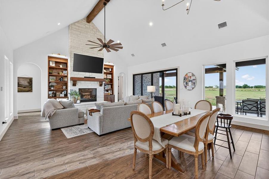 Spacious open-concept living area featuring a stone-clad fireplace with a wood mantle, vaulted ceilings with an exposed wood beam, recessed lighting, and wood-finish flooring
