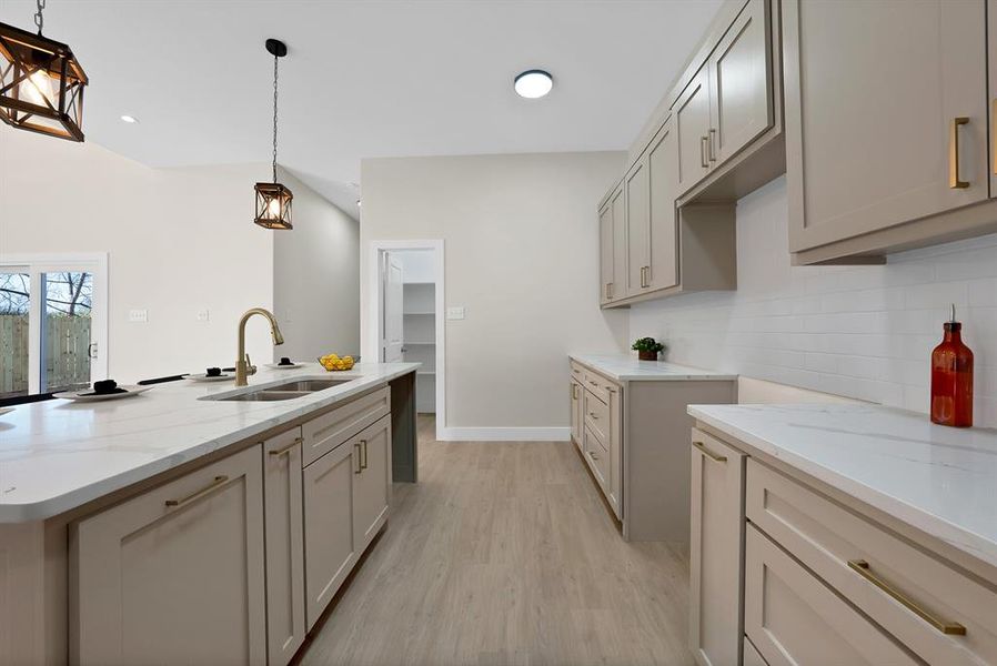 Kitchen with light stone counters, a kitchen island with sink, light wood-style floors, hanging light fixtures, and gray cabinetry