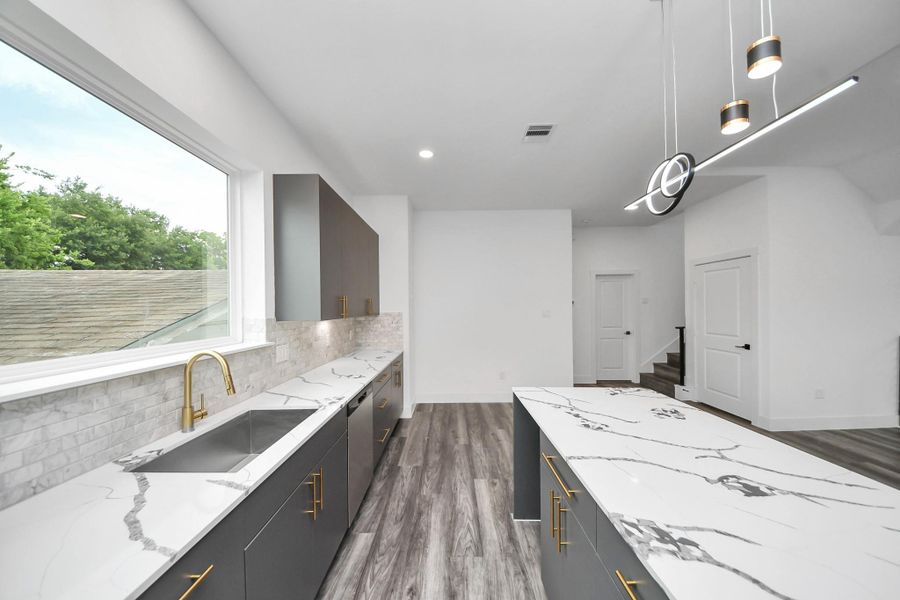 This modern kitchen features sleek, dark cabinetry with elegant gold handles, a spacious marble countertop with a matching island, and contemporary pendant lighting. The large window provides ample natural light, enhancing the bright and open atmosphere. This modern kitchen features sleek, dark cabinetry with elegant gold handles, a spacious marble countertop with a matching island, and contemporary pendant lighting. The large window provides ample natural light, enhancing the bright and open atmosphere.