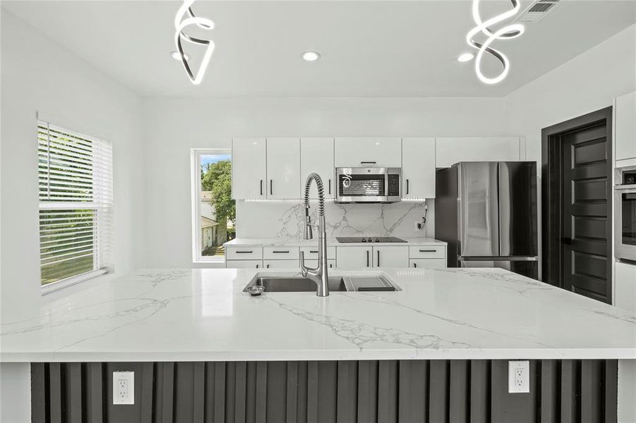 Kitchen featuring appliances with stainless steel finishes, white cabinets, backsplash, modern cabinets, and light stone counters Kitchen featuring appliances with stainless steel finishes, white cabinets, backsplash, modern cabinets, and light stone counters