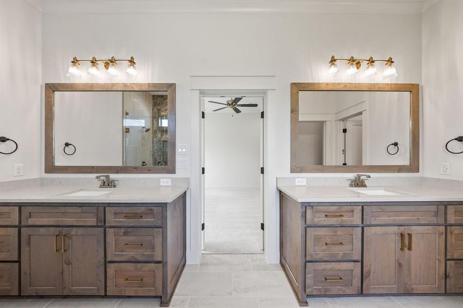 Dual vanities featuring wood-finish cabinetry, white countertops, and framed mirrors with brass-finish lighting