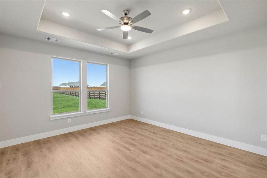 Empty room with light wood-type flooring, a tray ceiling, and ceiling fan