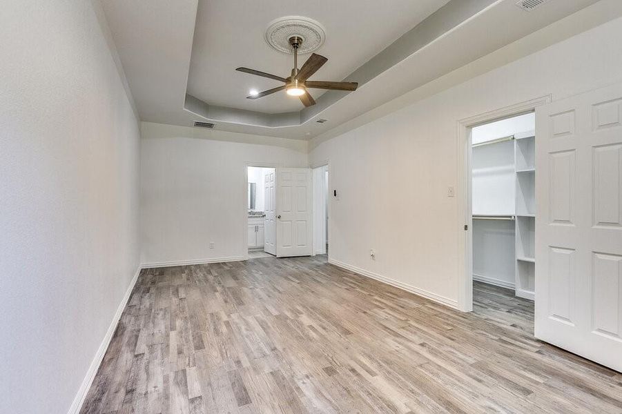 Unfurnished bedroom featuring light hardwood / wood-style flooring, a walk in closet, ceiling fan, and a raised ceiling