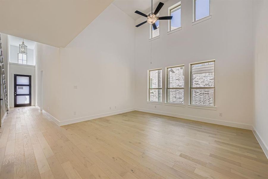 Unfurnished living room with light wood finished floors, a high ceiling, and ceiling fan Unfurnished living room with light wood finished floors, a high ceiling, and ceiling fan