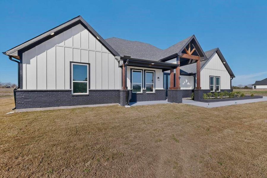 Modern inspired farmhouse featuring board and batten siding, a front yard, a porch, and brick siding Modern inspired farmhouse featuring board and batten siding, a front yard, a porch, and brick siding
