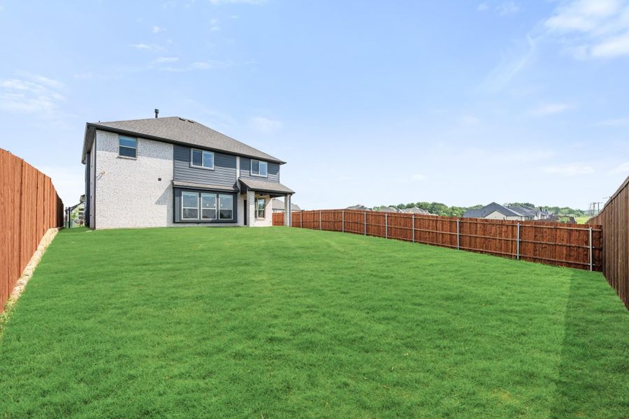 Backyard of two-story home with large green lawn and wood privacy fence on three sides