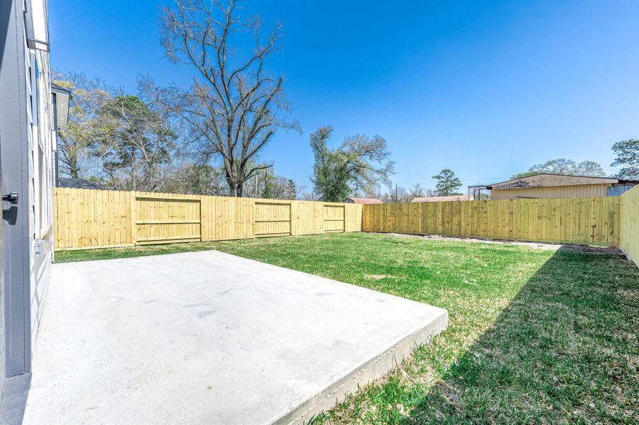 Spacious backyard featuring a concrete patio slab, fully fenced yard, and plenty of green space for outdoor living.