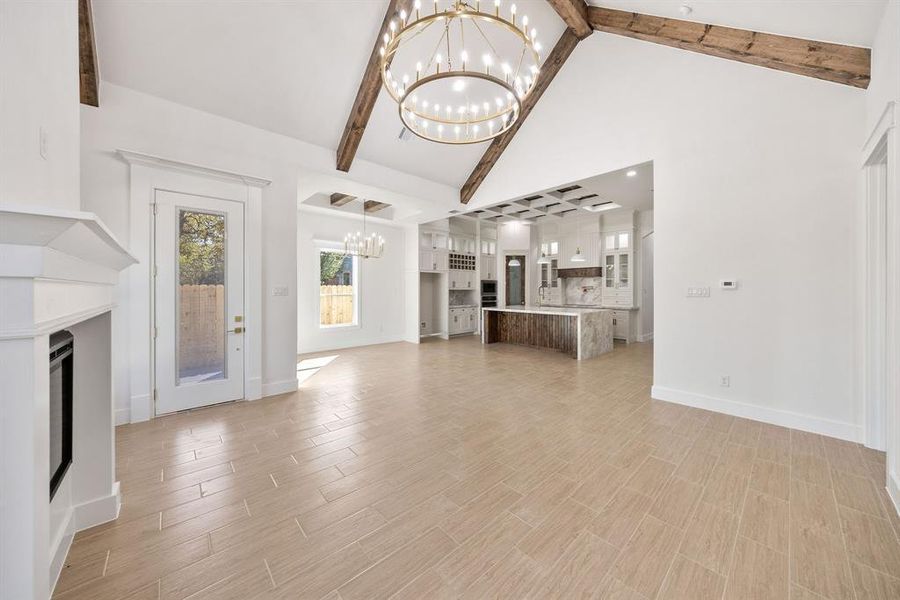 Unfurnished living room featuring a fireplace, a chandelier, wood finish floors, high vaulted ceiling, and beamed ceiling