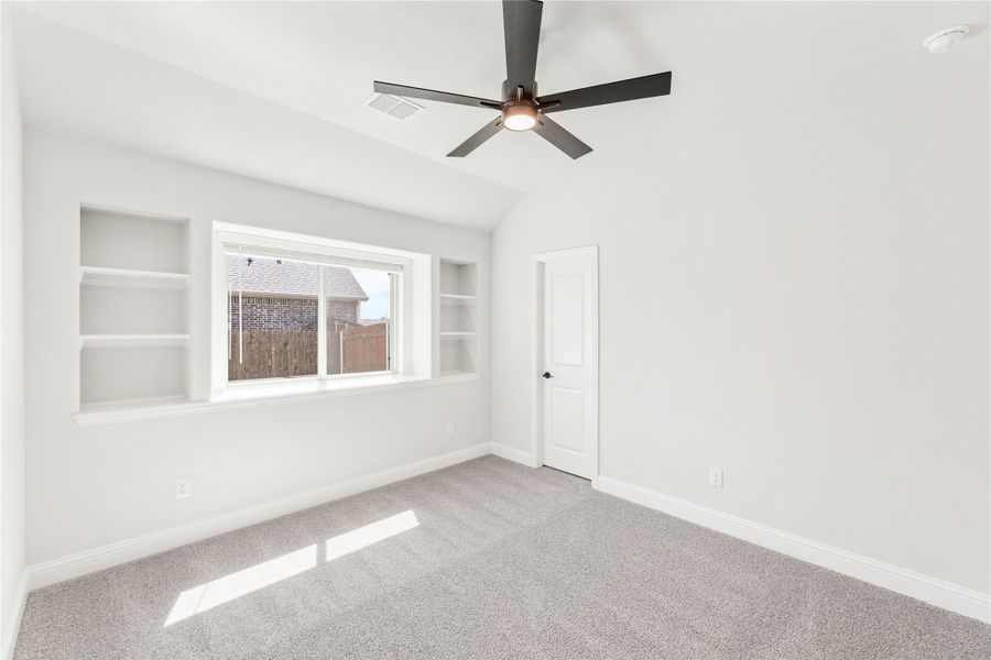 Empty bedroom with vaulted ceiling, ceiling fan, built-in shelves, and carpet flooring