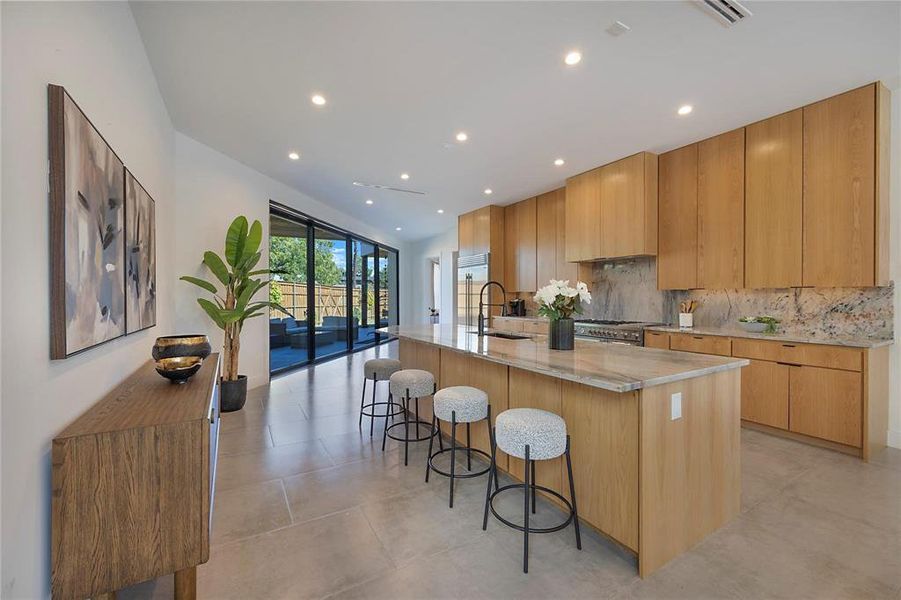 Kitchen with light stone countertops, a spacious island, sink, backsplash, and a kitchen breakfast bar