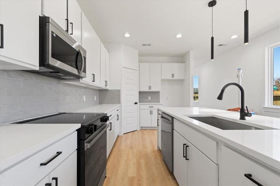 Kitchen featuring light wood finished floors, stainless steel appliances, light countertops, decorative backsplash, and a sink