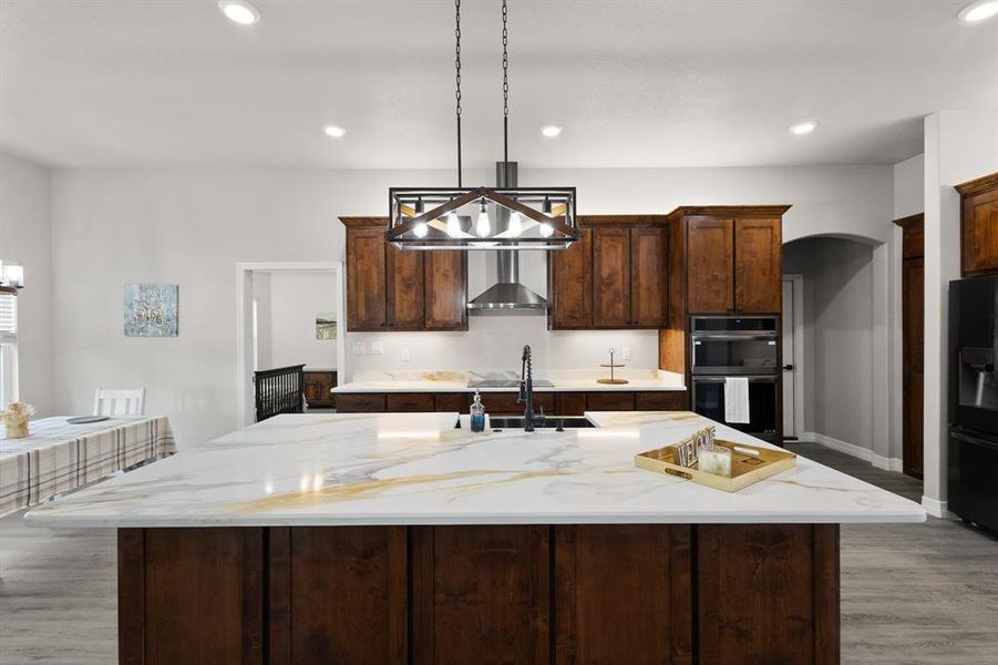 Kitchen with light wood-type flooring, light stone countertops, an island with sink, and recessed lighting