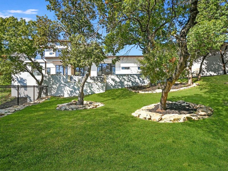 A tiered landscape with verdant grass and mature trees defines this property's serene outdoor space. A tiered landscape with verdant grass and mature trees defines this property's serene outdoor space.