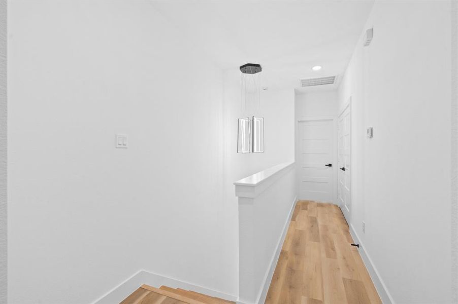 Hallway that leads to primary bedroom, custom light fixture above stairs