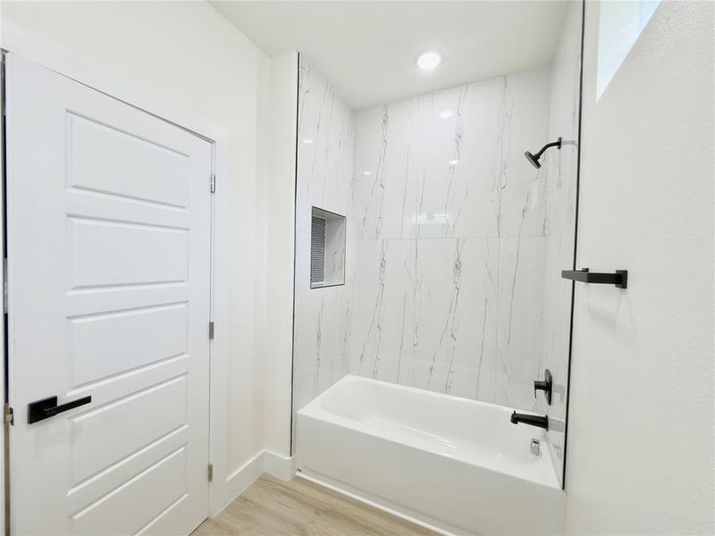 Modern bathroom featuring a white bathtub with matte black fixtures, full-height marble-look tile surround, a built-in shower niche, and a clear glass shower panel