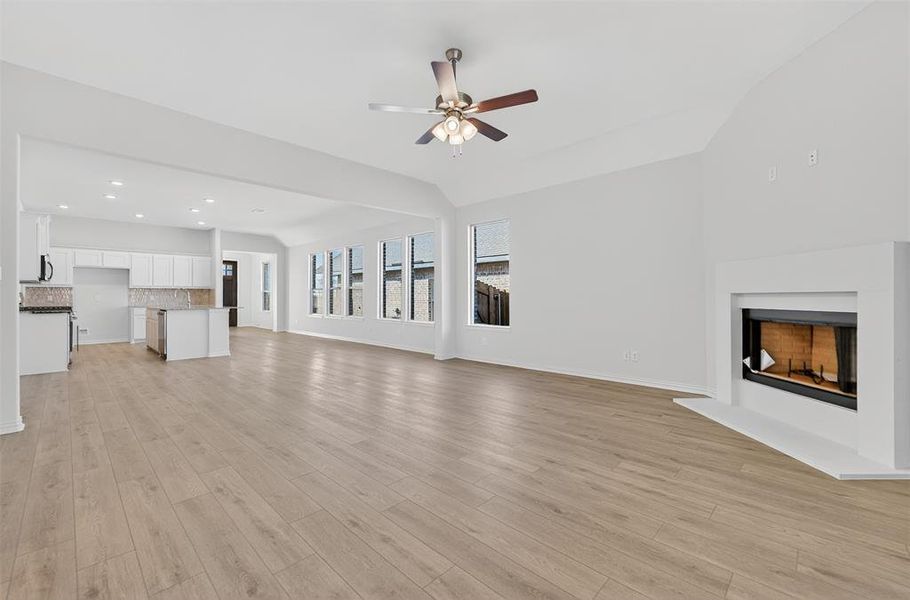 Unfurnished living room featuring a fireplace with raised hearth, light wood-style floors, recessed lighting, a ceiling fan, and vaulted ceiling
