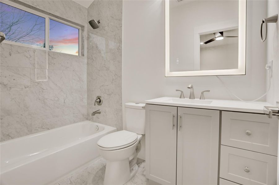 Stylish ensuite bath with shower/tub combo and modern fixtures including backlit vanity mirror..