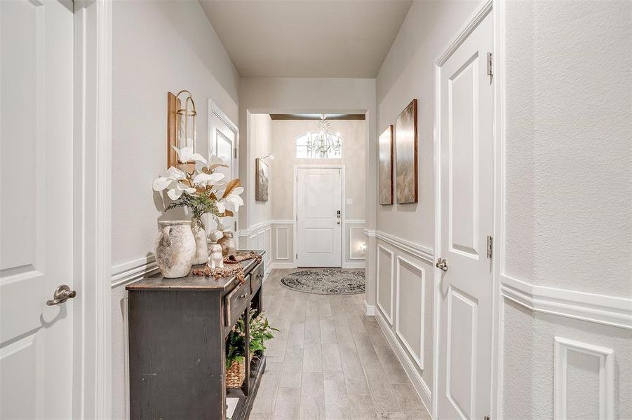 Doorway to outside featuring light wood-style floors, a decorative wall, an inviting chandelier, and wainscoting