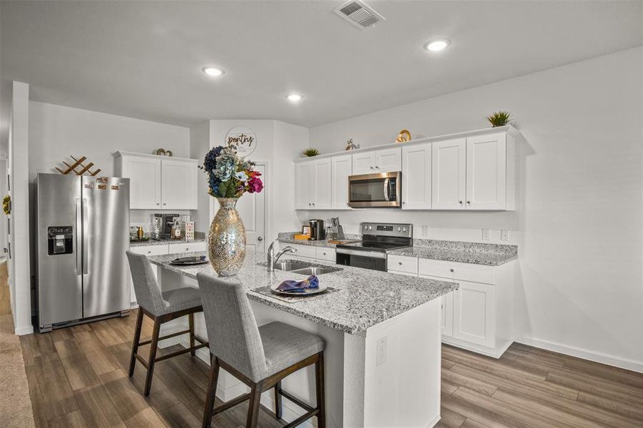 Kitchen featuring stainless steel appliances, a kitchen breakfast bar, a kitchen island with sink, white cabinetry, and recessed lighting