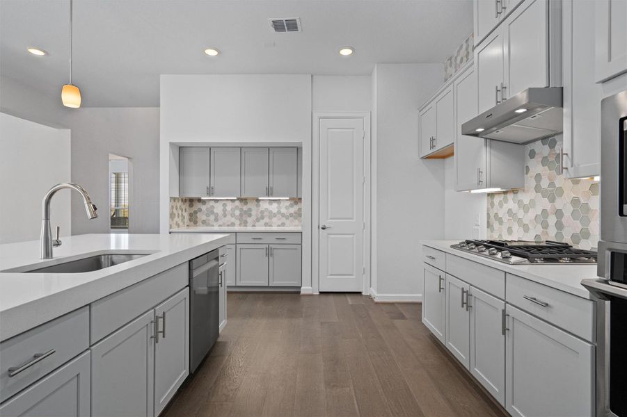 Kitchen with pendant lighting, stainless steel appliances, dark wood-type flooring, backsplash, and light stone counters Kitchen with pendant lighting, stainless steel appliances, dark wood-type flooring, backsplash, and light stone counters