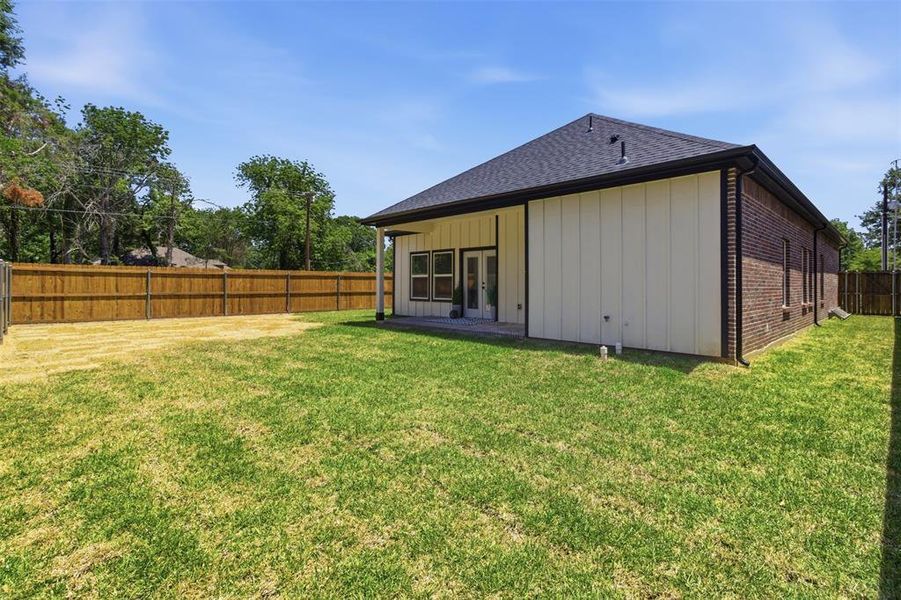 Spacious backyard featuring a full privacy fence, covered patio, white vertical siding, and brick exterior
