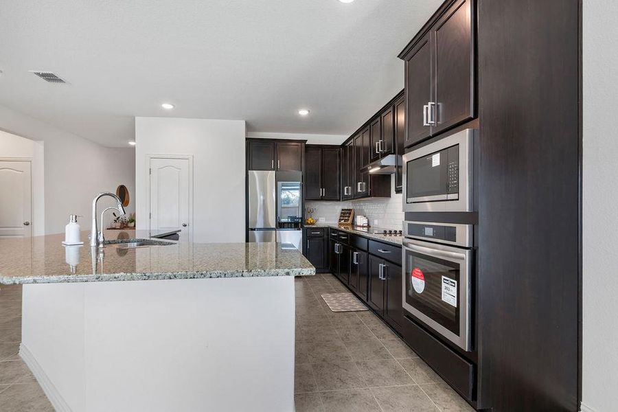 Kitchen featuring light stone counters, an island with sink, backsplash, stainless steel appliances, and recessed lighting Kitchen featuring light stone counters, an island with sink, backsplash, stainless steel appliances, and recessed lighting