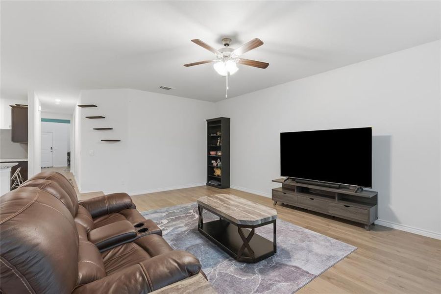 Open-concept living space featuring wood-finish flooring, a ceiling fan with light, and a built-in media console