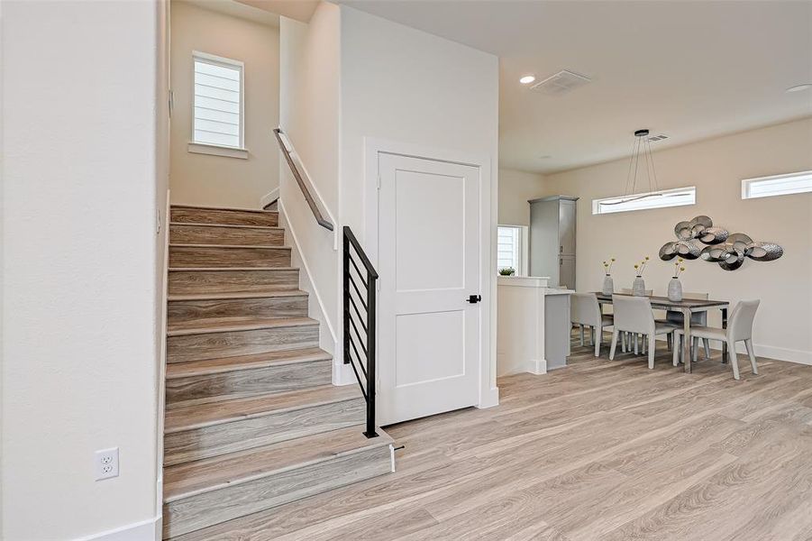 This photo showcases a modern, open-concept dining area with light wood flooring and contemporary decor. A staircase with a sleek railing leads upwards, and the space is well-lit with large windows and stylish lighting fixtures.