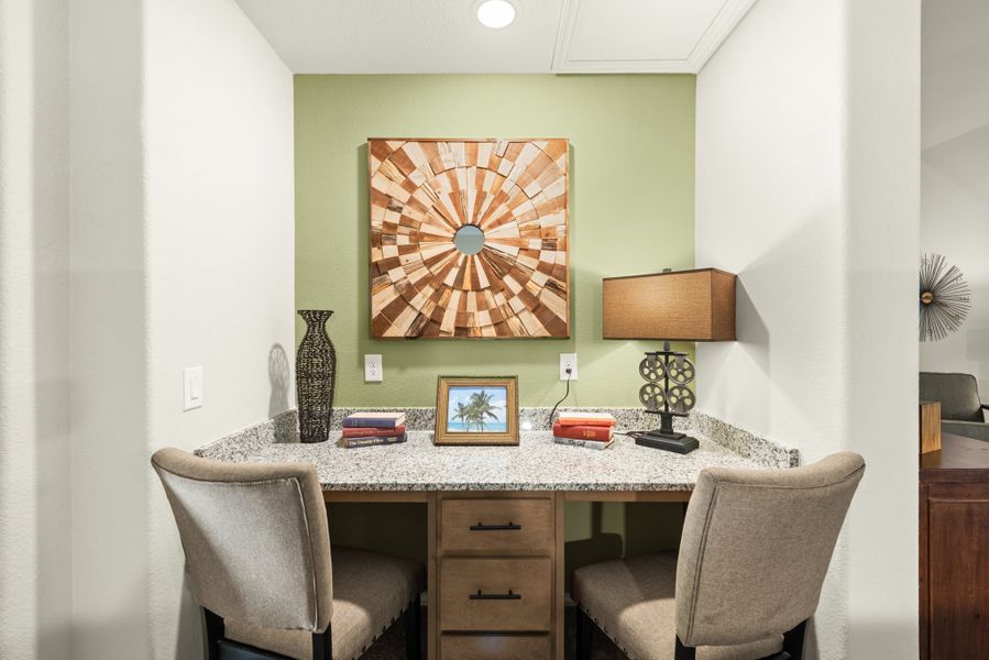 Built-in home office nook with granite desk, two chairs, and green accent wall with wood artwork above