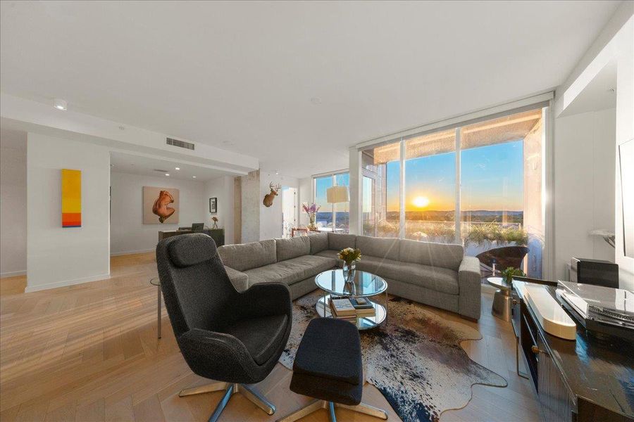 A generous corner living room wrapped in floor-to-ceiling glass, offering uninterrupted Hill Country and sunset vistas. The upgraded herringbone wood floors and open, gallery-like layout create a warm, modern backdrop for both relaxed evenings and elevated entertaining.