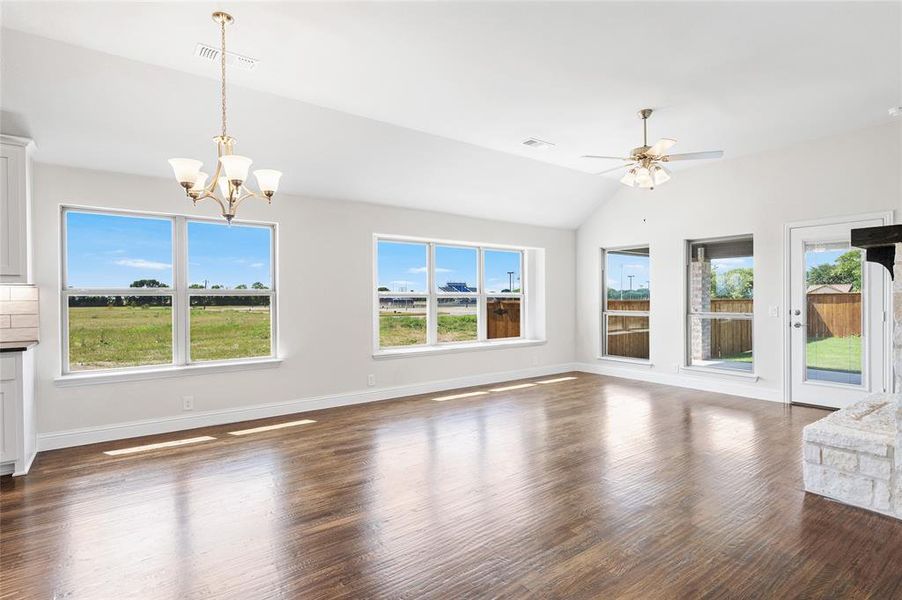 Unfurnished living room featuring dark wood-style flooring, lofted ceiling, a chandelier, and a ceiling fan Unfurnished living room featuring dark wood-style flooring, lofted ceiling, a chandelier, and a ceiling fan