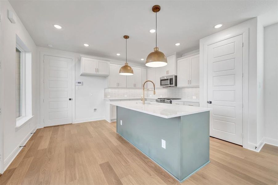 Open-concept kitchen featuring a central island with a light blue-grey finish, white countertops, stainless steel appliances, white cabinetry, and wood-finish flooring