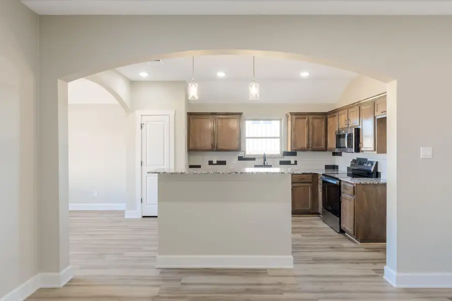 Kitchen with arched walkways, stainless steel appliances, hanging light fixtures, a center island, and vaulted ceiling