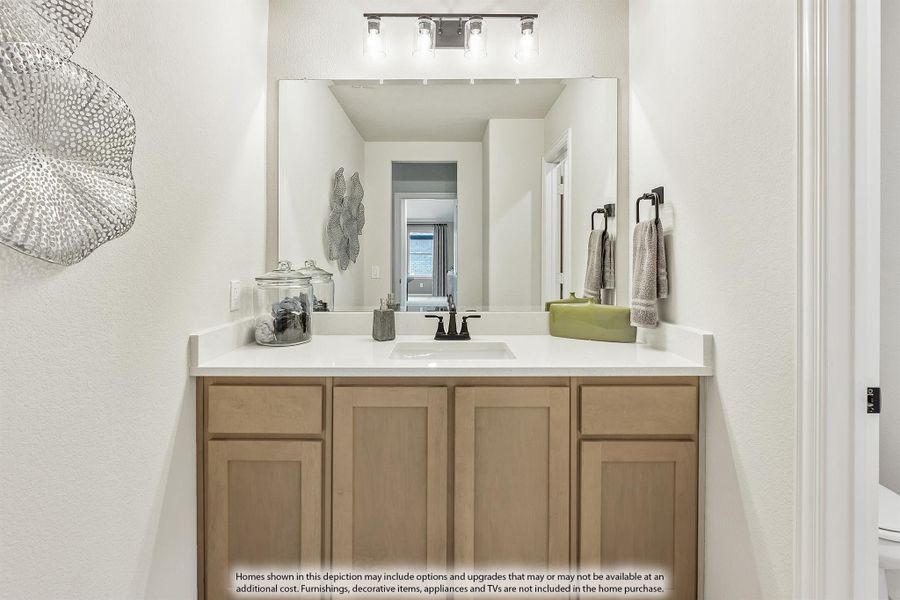 Bathroom vanity with light wood cabinets, white countertop, single sink, and large mirror with overhead lighting
