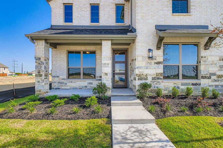 Entrance to property with a porch, stone siding, a shingled roof, and brick siding