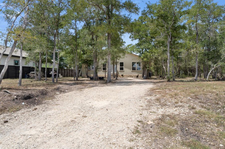 View of property hidden behind natural elements with stucco siding and dirt driveway View of property hidden behind natural elements with stucco siding and dirt driveway