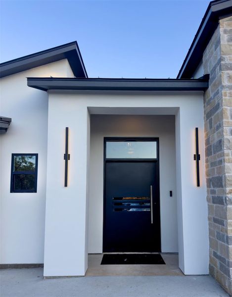 An inviting front entry showcases a modern dark door framed by stone and stucco finishes. An inviting front entry showcases a modern dark door framed by stone and stucco finishes.