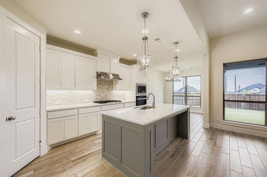Kitchen with white cabinetry, tasteful backsplash, hanging light fixtures, gray cabinetry, and light wood-style floors