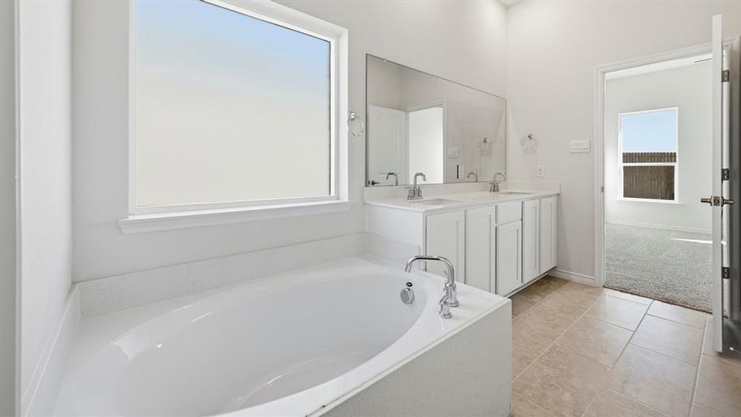 Soaking tub with chrome fixtures, dual vanity with white cabinetry, large mirror, and tile flooring