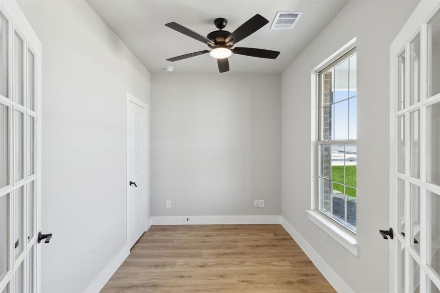 Empty room featuring visible vents, light wood finished floors, baseboards, ceiling fan, and french doors