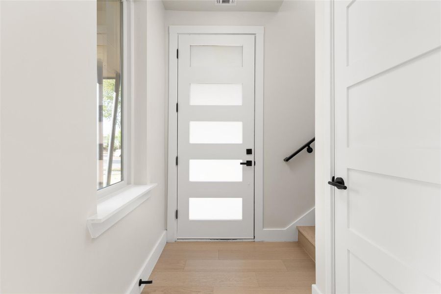 Natural light washes over the entry hallway featuring light wood floors and clean modern lines.