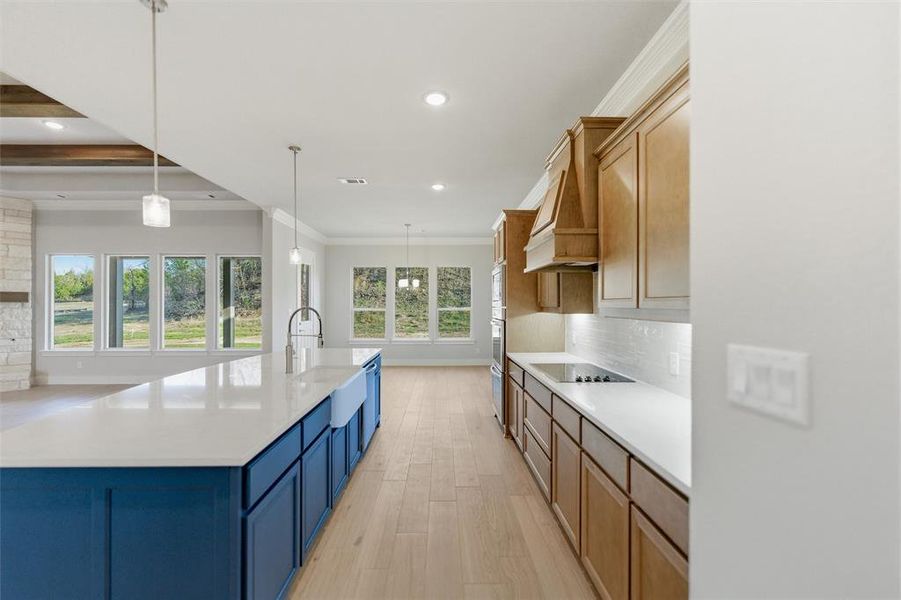 Dual tone kitchen featuring decorative backsplash, light wood-style flooring, dual tone cabinets, a large island with sink, and hanging light fixtures