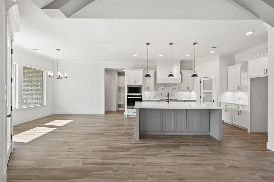 Kitchen featuring decorative light fixtures, ornamental molding, gray cabinetry, a center island with sink, and light wood-type flooring