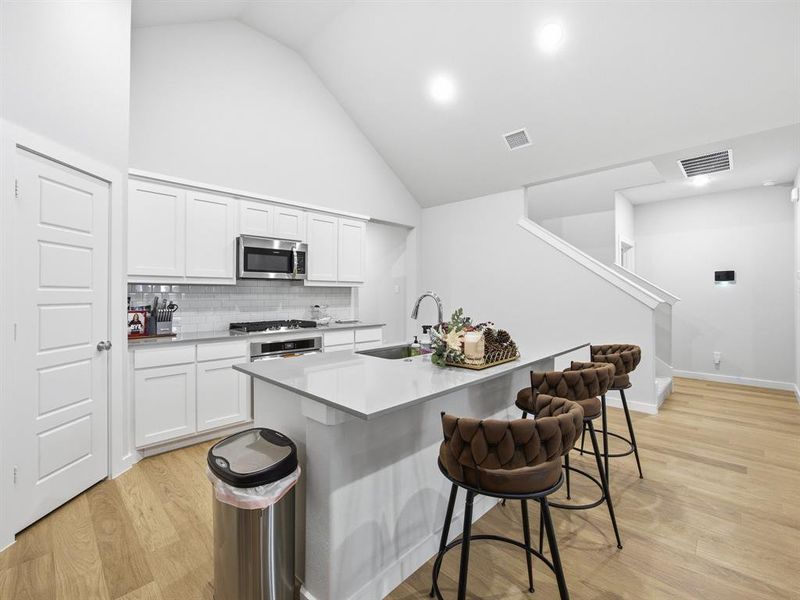 Kitchen featuring light wood-style flooring, a kitchen island with sink, a breakfast bar, white cabinets, and high vaulted ceiling