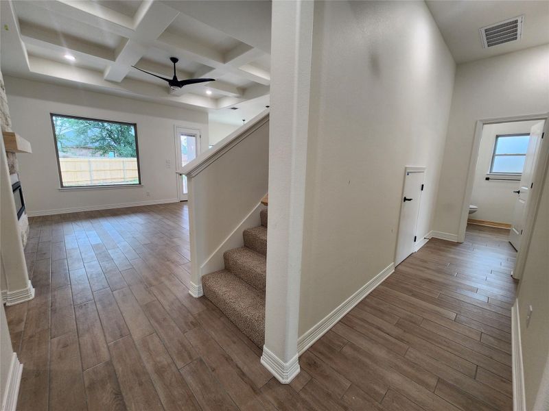 Open concept living space featuring wood-finish tile flooring, a coffered ceiling with recessed lighting and a ceiling fan, and a stone-clad fireplace with a wood mantel