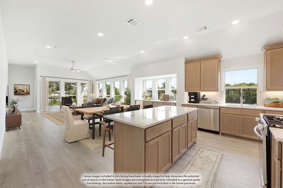 Open-concept kitchen with large island, light wood cabinets, and view into dining and living areas with vaulted ceiling