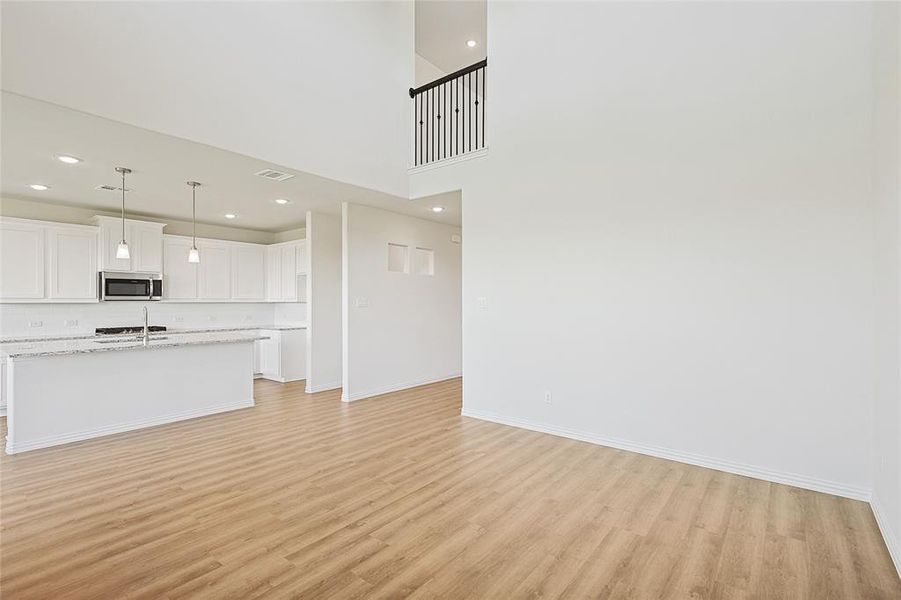 Unfurnished living room featuring sink, light hardwood / wood-style flooring, and a towering ceiling